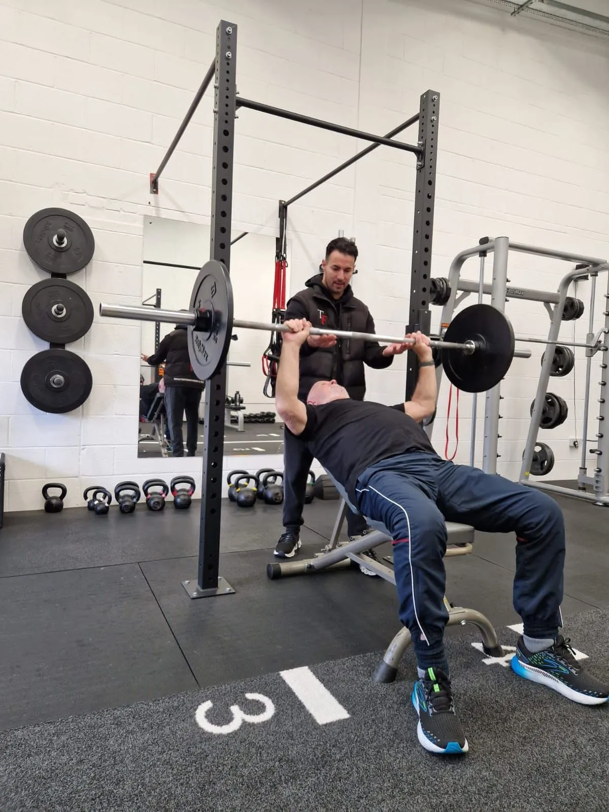 Client performing a barbell bench press while a Tiro Fitness trainer spots them